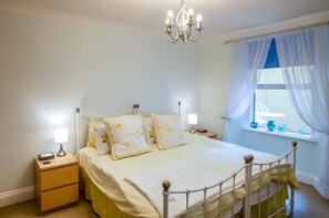Un dormitorio con cama, lámparas de noche, mesita de noche, ventana con cortinas y candelabro.