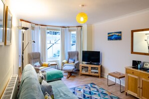 Una sala de estar con un sofá, dos sillones, un televisor, un mueble y una ventana con cortinas.