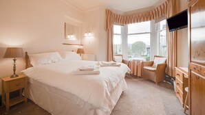 A hotel room with a large bed, bedside lamps, a small table, a chair, and a TV. - 6 Bed in Keswick (oc-ld177) (Keswick)