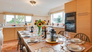 A well-lit kitchen with modern appliances, a dining table set for six with plates, glasses, and a vase of sunflowers. - 6 Bed in Keswick (oc-ld177) (Keswick)