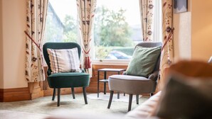 A cozy room with a green armchair and a grey armchair, a small table, and floral curtains. - 6 Bed in Keswick (oc-ld177) (Keswick)