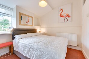 A bedroom with a large bed, a window with a view, and two wall-mounted paintings of flamingos. - 4 Bed in Tenby (oc-pw9281) (Tenby)