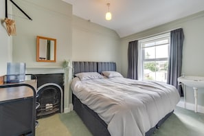 A bedroom with a bed, a fireplace, a desk, a mirror, and a window with curtains. - 4 Bed in Tenby (oc-pw9281) (Tenby)