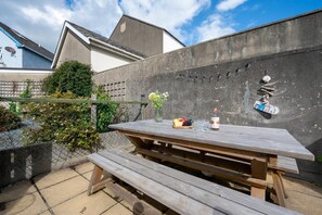A wooden picnic table with benches, a small table with a fruit bowl, glasses, and a bottle. - 4 Bed in Tenby (oc-pw9281) (Tenby)