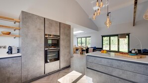 Een moderne keuken met inbouwapparatuur, een eethoek met veel natuurlijk licht, en een groot raam met uitzicht op de omgeving.