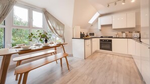 Eine moderne Küche mit weißen Schränken, einem Holzespeisesaal mit Bänken und einem großen Fenster mit Vorhängen.