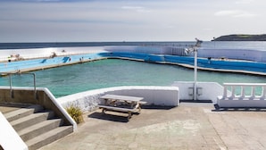 Piscina costiera con vista sul mare, scalini che conducono alla piscina e tavolo da picnic.