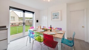 A dining area with a table set for four, colorful chairs, a bottle of wine, and a framed picture on the wall. - 4 Bed in Sandsend (oc-wa330) (Sandsend)
