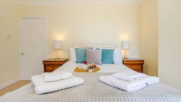A hotel room with a bed, two bedside tables, a door, and a nightstand with a lamp.