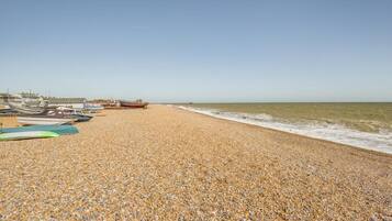 A pebble beach with boats and a clear sky.