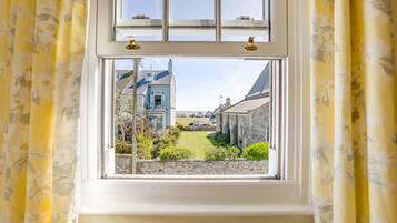 A window with a view of a building, a lawn, and a stone wall.