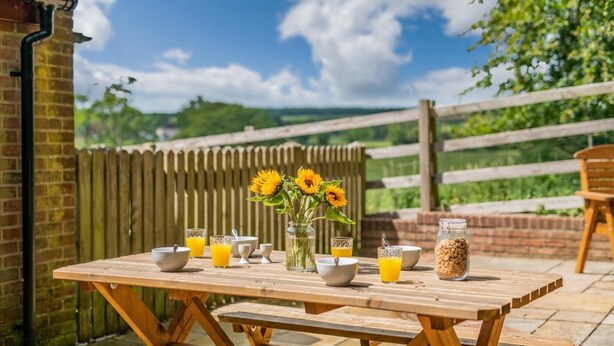 A wooden picnic table with bowls, glasses of orange juice, a vase with sunflowers, and a jar of cereal. - 2 Bed in Sledmere (oc-ey103) (Sledmere)