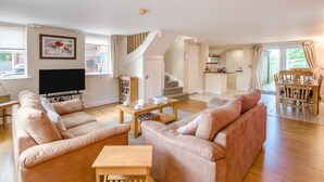 A spacious living room with a sofa set, a TV, and a bookshelf. A staircase leads to a kitchen area. - 2 Bed in Sledmere (oc-ey103) (Sledmere)