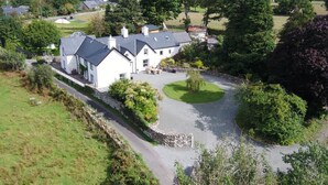 A large white house with a grey roof, surrounded by a well-maintained lawn and trees. - 4 Bed in Brithdir (oc-wag722) (Brithdir)