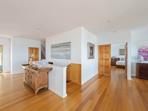 A spacious room with wooden flooring, a kitchen area with a wooden cabinet, and a bed in the background.