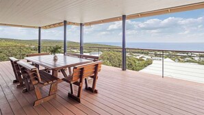 Um deck de madeira com mesa e bancos, com vista para uma paisagem com colinas e um corpo d'água.