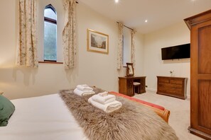Ein Schlafzimmer mit einem Bett, einem Schminktisch, einem Fernseher und einem Fenster mit Vorhängen.