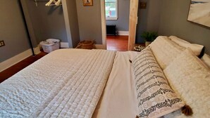 Een slaapkamer met een groot bed, een garderobe, een ingelijst kunstwerk aan de muur, en een deur die leidt naar een andere kamer.