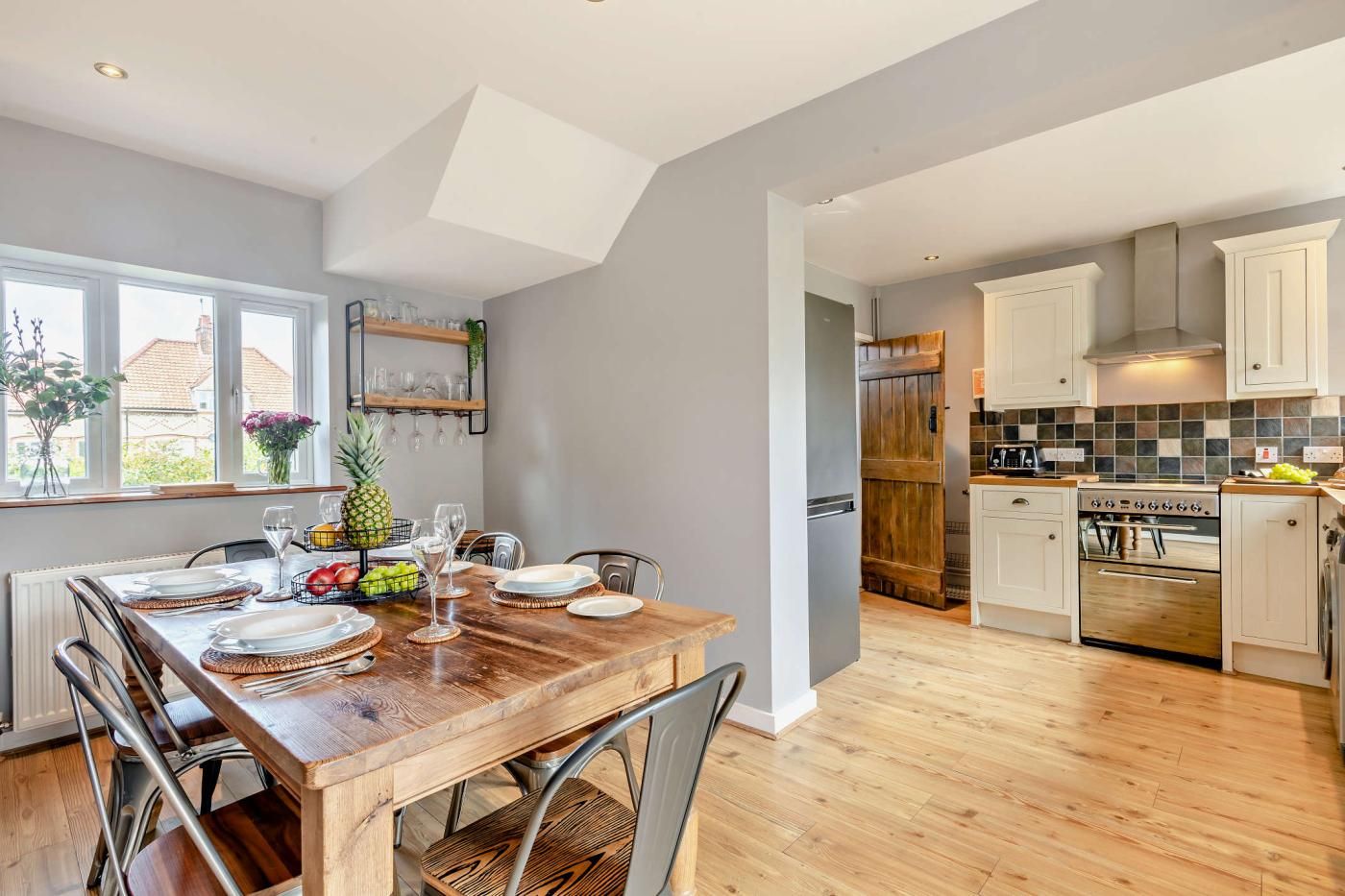 A modern kitchen with wooden flooring, white cabinets, and a dining area with a wooden table set for four.