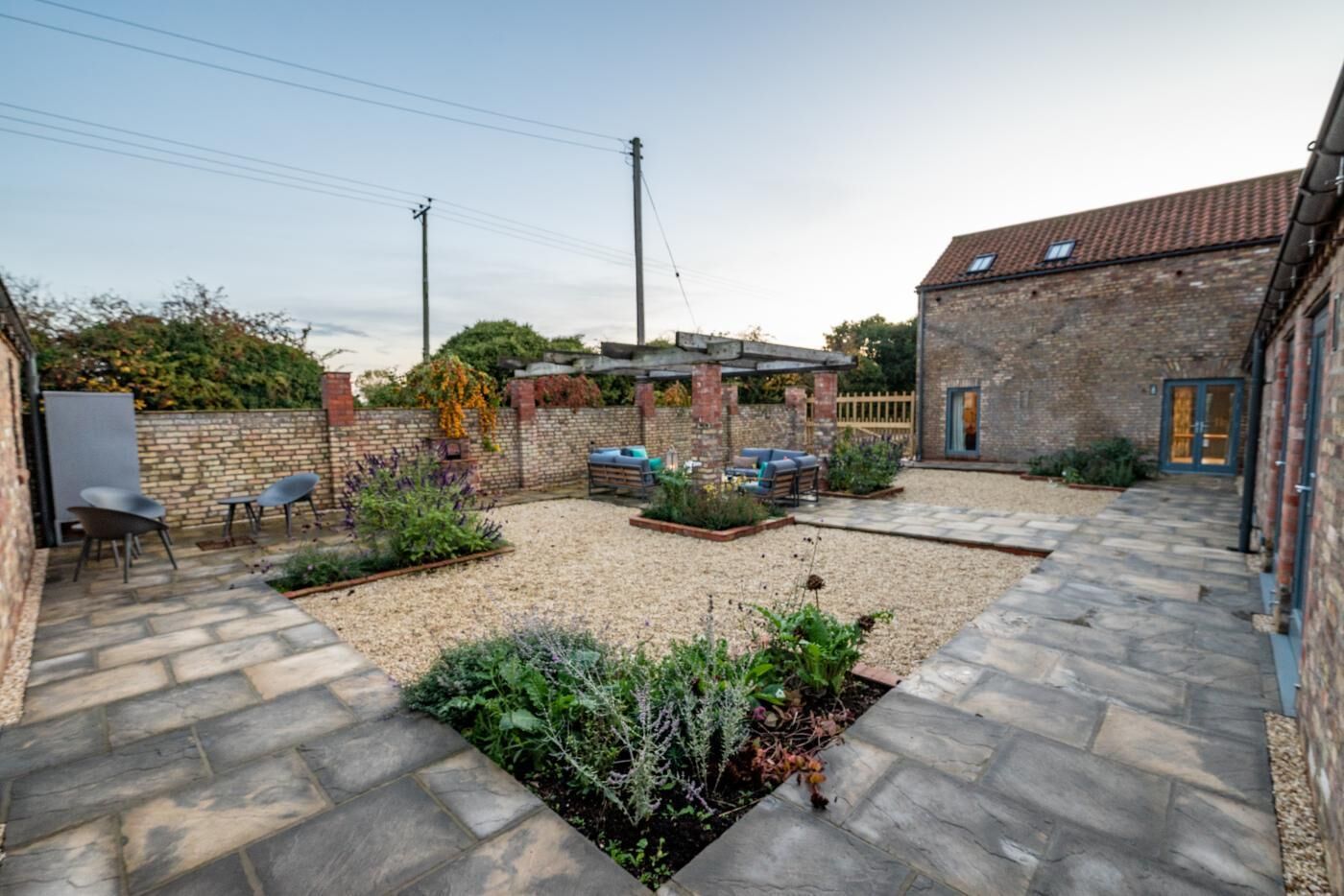 A courtyard with a stone patio, outdoor seating, a brick building, and a pergola.