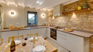 A modern kitchen with a stone wall backsplash, a dining area with a table set for a meal, and a window providing natural light. - 3 Bed in Holme-on-Spalding-Moor (oc-vy213) (Holme-on-Spalding-Moor)