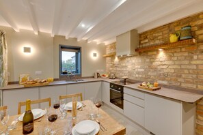 A modern kitchen with a stone wall backsplash, a dining area with a table set for a meal, and a window providing natural light. - 3 Bed in Holme-on-Spalding-Moor (oc-vy213) (Holme-on-Spalding-Moor)