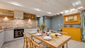 A modern kitchen with a dining area, featuring a brick wall, wooden cabinets, and a dining table set for a meal. - 3 Bed in Holme-on-Spalding-Moor (oc-vy213) (Holme-on-Spalding-Moor)