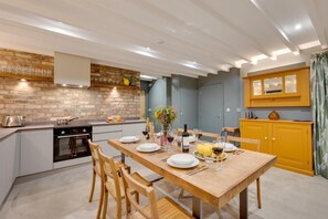 A modern kitchen with a dining area, featuring a brick wall, wooden cabinets, and a dining table set for a meal. - 3 Bed in Holme-on-Spalding-Moor (oc-vy213) (Holme-on-Spalding-Moor)