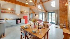 A spacious kitchen with wooden beams, a dining area with a table set for four, and a cozy living space with a sofa and curtains. - 2 Bed in Holme-on-Spalding-Moor (oc-vy215) (Holme-on-Spalding-Moor)