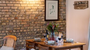 A dining area with a brick wall, wooden ceiling beams, a table set for four, and a framed picture on the wall. - 2 Bed in Holme-on-Spalding-Moor (oc-vy215) (Holme-on-Spalding-Moor)