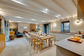 A dining area with a long table set for a meal, a kitchen area with a sink and countertop, and a living space with a sofa and television. - 7 Bed in Holme-on-Spalding-Moor (oc-vy216) (Holme-on-Spalding-Moor)