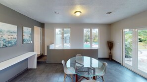 Un interior moderno con una mesa de vidrio, sillas blancas, un banco y ventanas amplias.