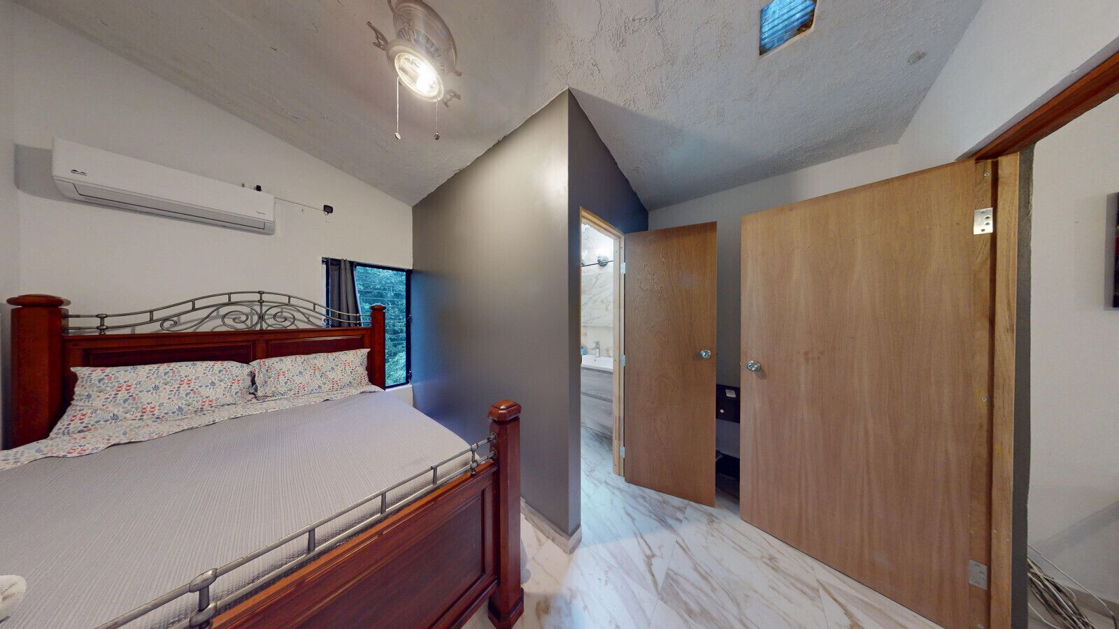 Un dormitorio con cama de madera, ventilador de techo y ventana con vista a árboles.