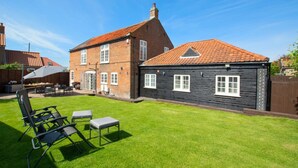 Une maison à deux étages, avec un toit recouvert de tuiles rouges, une façade en briques et une pelouse bien entretenue.