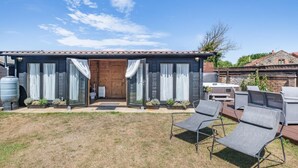 Une maison avec une porte d’entrée, deux portes-fenêtres coulissantes, un patio avec des meubles d’extérieur et un réservoir d’eau.