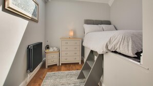 Une chambre avec un lit en mezzanine, une table de chevet avec une lampe, un radiateur et un tableau encadré au mur.