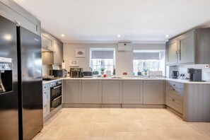 A modern kitchen with grey cabinets, a stainless steel refrigerator, a built-in oven, a microwave, and a coffee maker. - 8 Bed in Bacton (oc-2383) (Bacton)