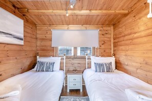 Habitació d'una cabana de fusta amb dos llits, una taula petita i una finestra.