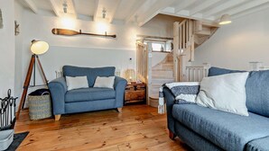 Ein gemütliches Wohnzimmer mit einem blauen Sofa, Holzboden und einer Treppe, die zu einer oberen Ebene führt.
