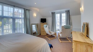 Ett hotellrum med en stor säng, två gungstolar, en tv och en byrå.