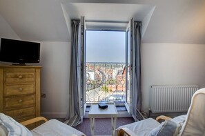 A hotel room with a television, a small table, two beds, a window with curtains, and a radiator. - 3 Bed in Swanage (oc-wy446) (Swanage)