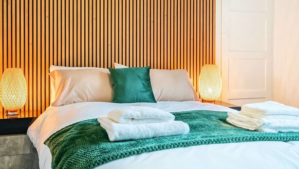 A neatly made bed with white and green linens, two bedside lamps, and a green throw blanket. - 4 Bed townhouse Swansea city centre (Swansea)