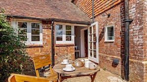A brick building with a tiled roof, a wooden table with chairs, and a door leading inside. - 3 Bed in Benenden (oc-cb671) (Benenden)