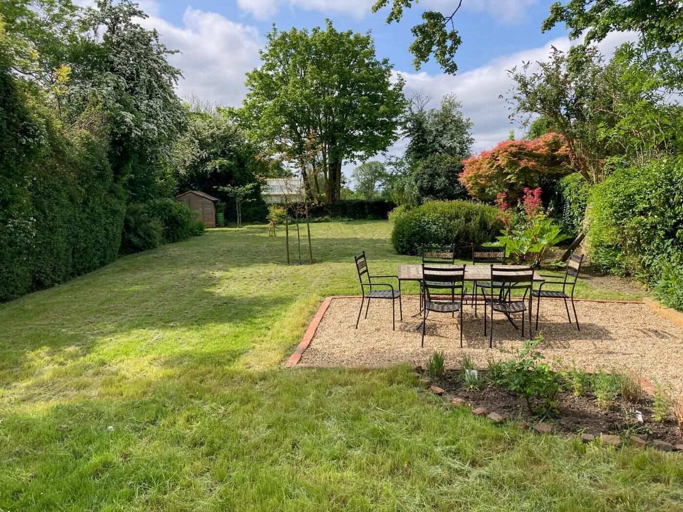 A garden with a gravel patio, a wooden table, and chairs.