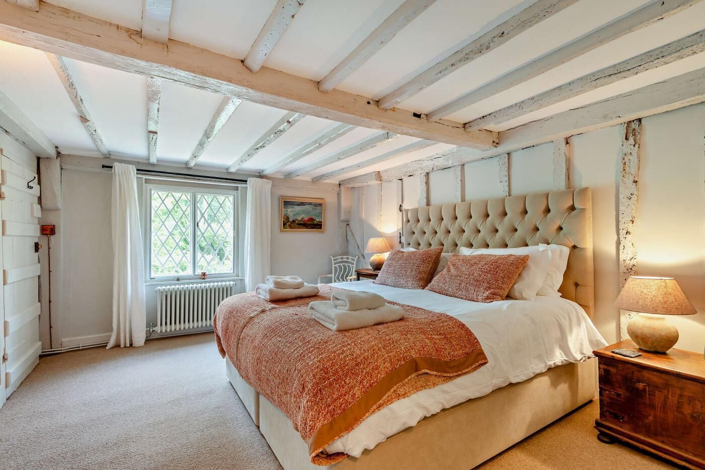 Une chambre à coucher avec un grand lit, une fenêtre avec des rideaux, un radiateur et une table de chevet en bois avec une lampe.
