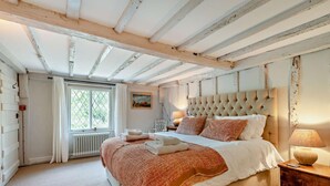 A bedroom with a large bed, a window with curtains, a radiator, and a wooden nightstand with a lamp. - 3 Bed in Benenden (oc-cb671) (Benenden)