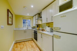 Eine kleine Küche mit weißen Schränken, einem eingebauten Backofen und einem weißen Kühlschrank mit dem Aufdruck 'Amica'.