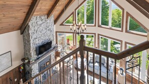 Un vaste espace de vie agrémenté d’une cheminée en pierre, de grandes fenêtres et d’un escalier en bois.