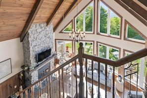 A spacious living area with a stone fireplace, large windows, and a wooden staircase.