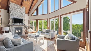 A spacious living room with a stone fireplace, multiple seating areas, and large windows offering a view of the outdoors.